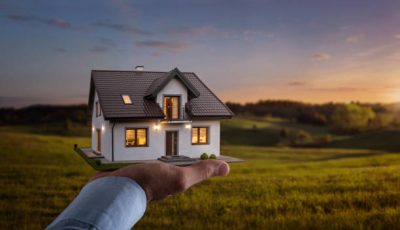 Concept of buying or building a new home. Male hand showing, offering a new dream house at the empty field with copy space