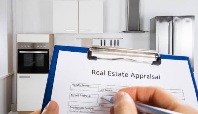 Close-up Of Person Hand Filling Real Estate Appraisal Document In Front Of House