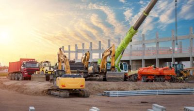 Many different multiclored colorful heavy industrial machinery equipment at construction site parking area against warehouse building city infrastructure development. Commercial vehicles rental sale.